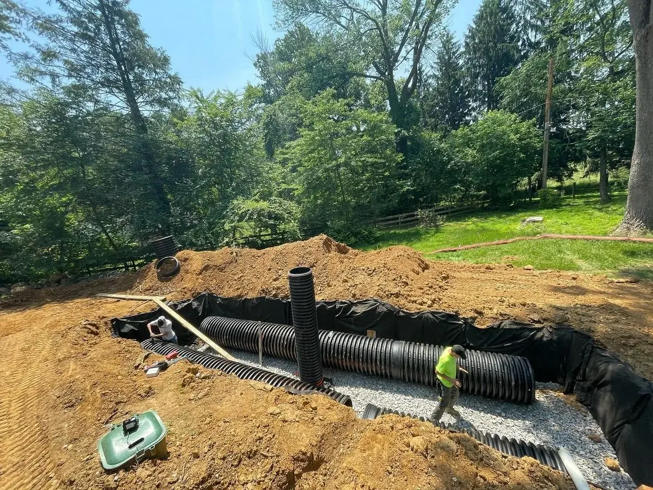Large stormwater infiltration bed with perforated pipe being installed in a lawn
